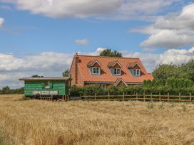 A red brick house with orange tiled roof next to a green wooden structure in a field of golden crops at Wayside Cottage in Pocklington
