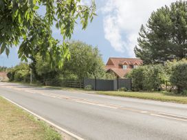 A road bordered by trees and bushes with a house and gate behind at Wayside Cottage in Pocklington