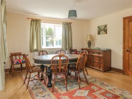 A dining room with a wooden table and chairs a sideboard with a lamp and a window with curtains at Wayside Cottage in Pocklington