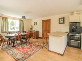 A dining area with a wooden table and six chairs a sideboard a kitchen island with a stool an oven and a window with green curtains at Wayside Cottage in Pocklington