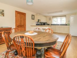 A dining area with wooden table and chairs next to a kitchen with white cabinets and a window at Wayside Cottage in Pocklington