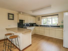 A kitchen with cream cabinets a countertop with two stools a window above the sink and a clock on the wall at Wayside Cottage in Pocklington
