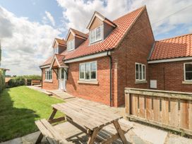 A brick house with a tiled roof and wooden picnic table in the garden at Wayside Cottage in Pocklington