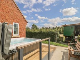 An outdoor area with a hot tub next to a brick house and a wooden bench near a green shed at Wayside Cottage in Pocklington