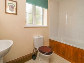 A bathroom with a toilet a bathtub with wooden paneling a sink and a window at Wayside Cottage in Pocklington