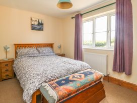 A bedroom with a double bed, two bedside tables with lamps, a window with purple curtains, and a wooden chest at the foot of the bed at Wayside Cottage in Pocklington