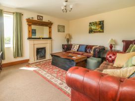 A living room with red leather sofas a wooden coffee table a fireplace and green curtains at Wayside Cottage in Pocklington