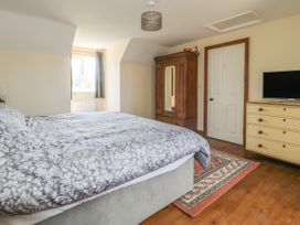 A bedroom with a bed a wooden wardrobe a dresser with a TV a rug on wooden floor and a window with curtains at Wayside Cottage in Pocklington