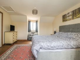 A bedroom with a bed beside a nightstand with a lamp a chair in front of a window a dresser with a TV and a rug on the floor at Wayside Cottage in Pocklington