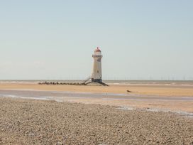 A lighthouse on a sandy beach with some people walking near it and wind turbines in the background at Beachway in Talacre near Prestatyn