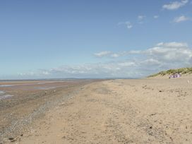 A sandy beach with scattered pebbles and grass-covered dunes under a blue sky at Beachway in Talacre near Prestatyn