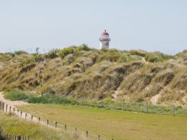 A grassy sand dune with a small lighthouse and wind turbines in the background at Beachway in Talacre near Prestatyn