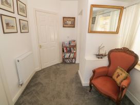 A corner with a red armchair and a small bookshelf next to a white door with framed pictures on the wall at Beachway in Talacre near Prestatyn