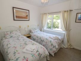 A bedroom with two single beds with floral bedding a nightstand and a window with curtains at Beachway in Talacre near Prestatyn