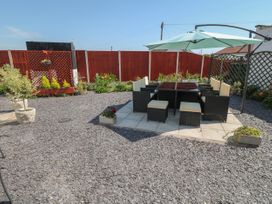 An outdoor patio area with a dining table set under a large umbrella surrounded by gravel and red wooden fencing at Beachway Talacre near Prestatyn