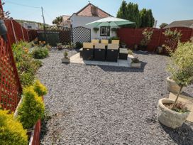 A backyard with gravel ground a table and chairs with an umbrella and potted plants and flowers at Beachway in Talacre near Prestatyn