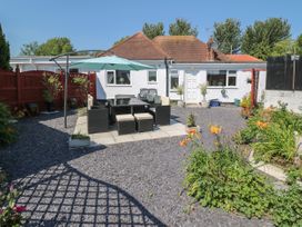 A backyard with outdoor dining furniture and umbrella on a paved area surrounded by gravel and flowers at Beachway in Talacre near Prestatyn