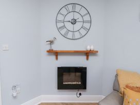 A living room featuring a clock, shelf, and electric fireplace at Hasting Dairy in North Sunderland near Seahouses