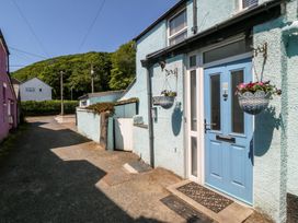 The exterior entrance of a blue house with a blue door and hanging flower baskets on a sunny day at Bay View Apartment in Porthmadog