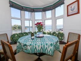 A dining area with a round table covered with a green and white patterned tablecloth surrounded by wooden chairs near large windows overlooking a waterfront at Bay View Apartment in Porthmadog