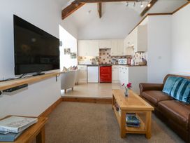 A living room with a brown leather sofa, wooden coffee table, wall mounted TV, and a kitchen with white cabinets and a red oven at Bay View Apartment in Porthmadog