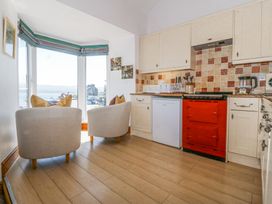 A kitchen with a red stove white cabinets two armchairs near a bay window overlooking a waterfront view at Bay View Apartment in Porthmadog