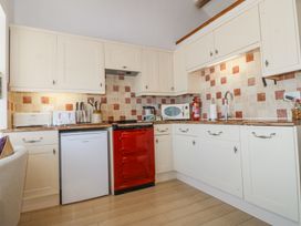 A kitchen with white cabinets red oven small white refrigerator toaster microwave and tiled backsplash at Bay View Apartment in Porthmadog