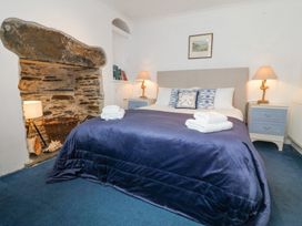 A bedroom with a bed covered in a blue blanket towels on bed two bedside tables with lamps and a stone fireplace at Bay View Apartment in Porthmadog