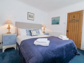 A bedroom with a double bed covered with a blue bedspread and folded white towels on top with two bedside tables with lamps and paintings on the wall at Bay View Apartment in Porthmadog