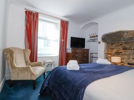 A bedroom with a bed covered with a blue blanket towels on the bed a beige armchair near a window with red striped curtains a television on a wooden dresser and a stone fireplace at Bay View Apartment in Porthmadog