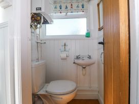 A small bathroom with a toilet, a wall-mounted sink, a window with a patterned blind, and a wooden door at Bay View Apartment in Porthmadog