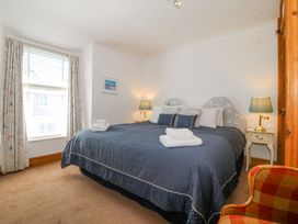A bedroom with a large bed with blue bedding two bedside tables with lamps a window with curtains and a checkered armchair at Bay View Apartment in Porthmadog