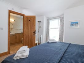 A bedroom with a bed covered in blue bedspread with white towels on it a wooden door leading to a bathroom a window with curtains and a framed picture on the wall at Bay View Apartment in Porthmadog