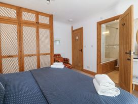 A bedroom with a bed covered in blue polka dot bedding with towels on top wooden wardrobe doors an armchair and an open door showing a bathroom at Bay View Apartment in Porthmadog