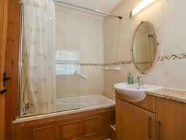 A bathroom with a bathtub shower combination a sink with a cabinet and an oval mirror at Bay View Apartment in Porthmadog