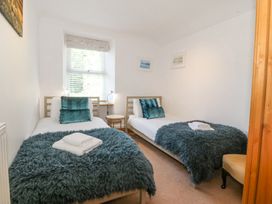 A bedroom with two single beds, teal blankets and pillows, a window with blinds, bedside lamps, a small round table and a chair at Bay View Apartment in Porthmadog