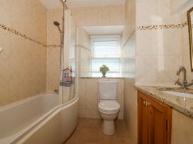 A bathroom with a bathtub shower combination a toilet and a sink with wooden cabinet at Bay View Apartment in Porthmadog