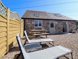 A stone building with two skylights a door two windows a wooden picnic table and two lounge chairs on a gravel area at Bwthyn Taid in Holywell