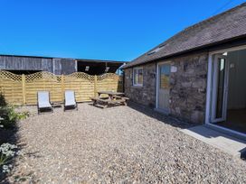 A stone building with an open door and a gravel yard with two lounge chairs and a wooden picnic table at Bwthyn Taid in Holywell