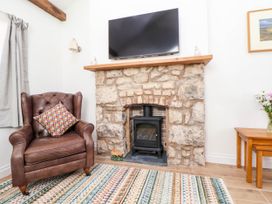 A living room with a leather armchair and a fireplace with a stove and a television above at Bwthyn Taid in Holywell