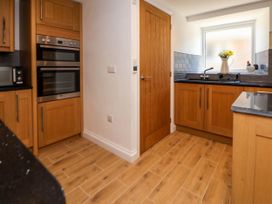 A kitchen with wooden cabinets a double oven a black countertop a sink under a window and a wooden door at Bwthyn Taid in Holywell