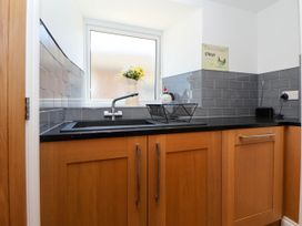 A kitchen sink with a faucet a window a vase with flowers a dish rack wooden cabinets and gray tiled backsplash at Bwthyn Taid in Holywell