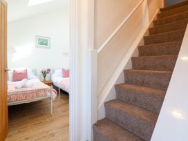 A carpeted staircase next to a bedroom with two beds and a vase of flowers on a wooden nightstand at Bwthyn Taid in Holywell