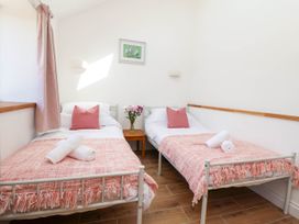 A bedroom with two single beds with pink pillows and blankets and a small wooden table with flowers between them at Bwthyn Taid in Holywell
