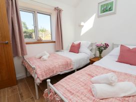 A bedroom with two single beds pink blankets and pillows a window wooden door and flowers on a bedside table at Bwthyn Taid in Holywell