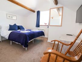 A bedroom with a bed covered with blue pillows and blanket a wooden rocking chair a mirror and a window at Bwthyn Taid in Holywell