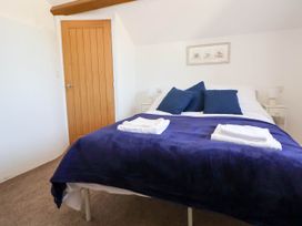 A bedroom with a bed covered in a blue blanket and pillows beside a wooden door at Bwthyn Taid in Holywell