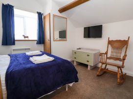 A bedroom with a bed covered by a blue blanket towels on the bed a wooden rocking chair a dresser with two drawers a wall-mounted TV a mirror and a window with blue curtains at Bwthyn Taid in Holywell