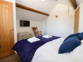 A bedroom with a bed covered with white and blue bedding a wooden rocking chair a wall-mounted television and a chest of drawers at Bwthyn Taid in Holywell