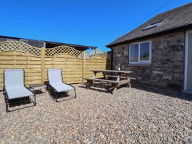 An outdoor patio area with two lounge chairs a small table a wooden picnic table with wine glasses and a bottle by a stone house at Bwthyn Taid in Holywell